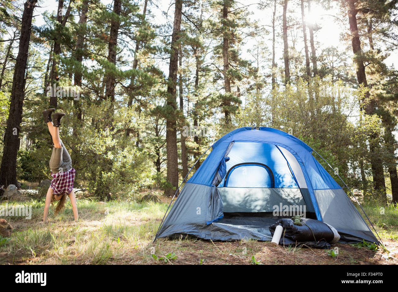 Carefree bionda camper facendo handstand accanto alla tenda Foto Stock