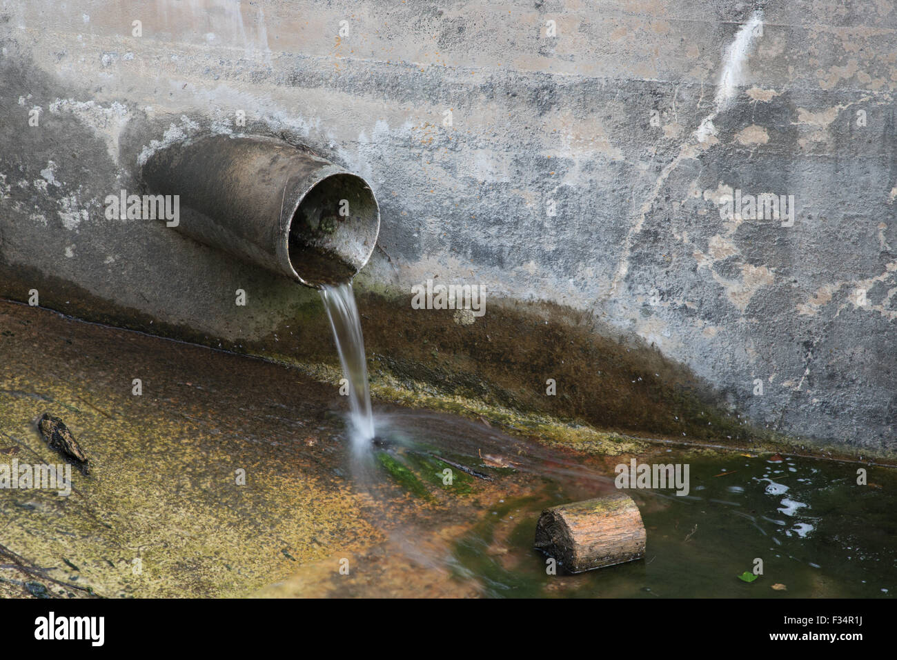 Tubo di drenaggio che sporge da una parete in cemento in un flusso. Foto Stock