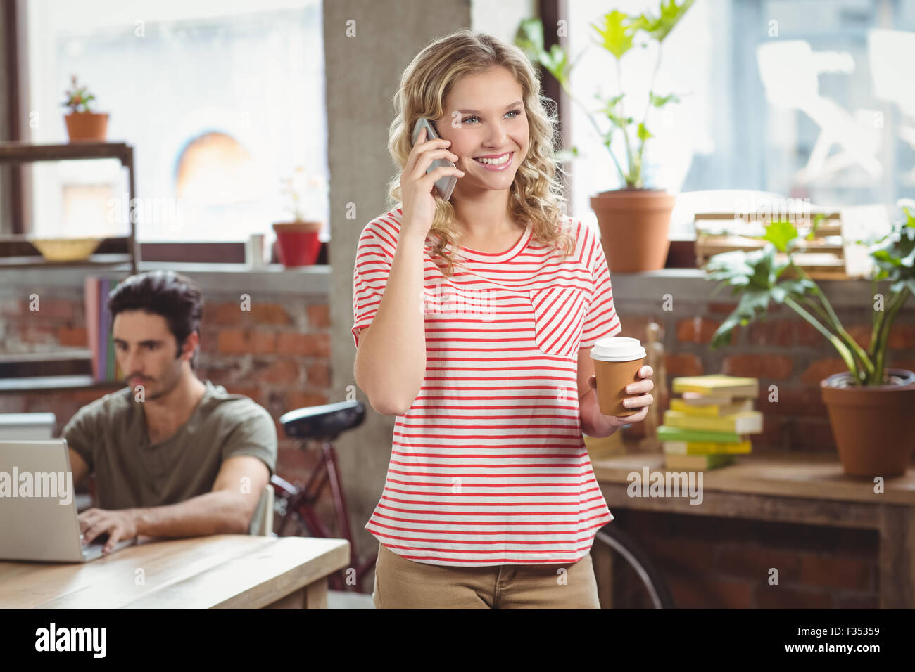 Felice imprenditrice di parlare al telefono tenendo il caffè in ufficio Foto Stock