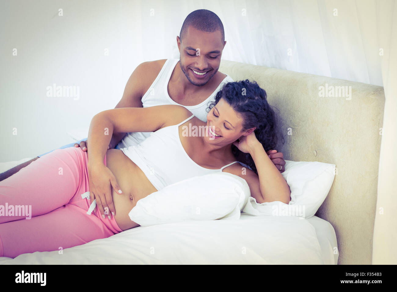 Felice moglie incinta con il marito sdraiato sul letto Foto Stock