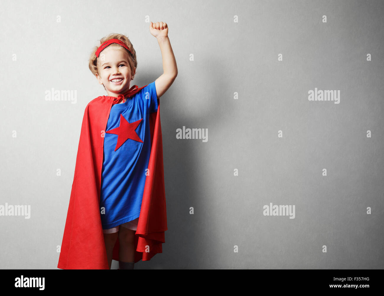 Bambino felice in tuta del supereroe contro il muro grigio. Foto Stock