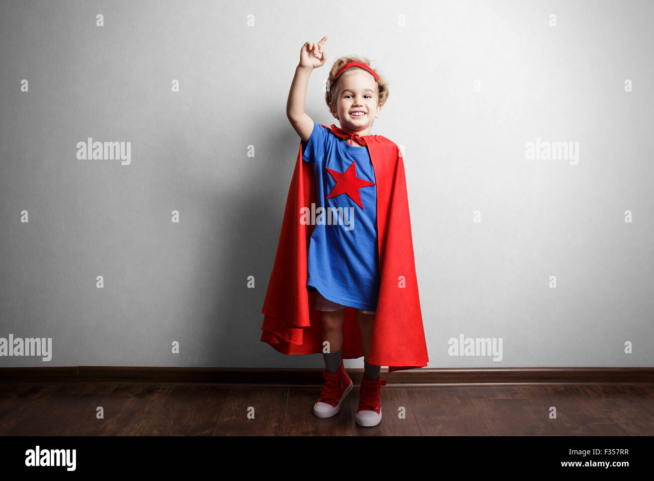 Bambino felice in tuta del supereroe contro il muro grigio. Foto Stock