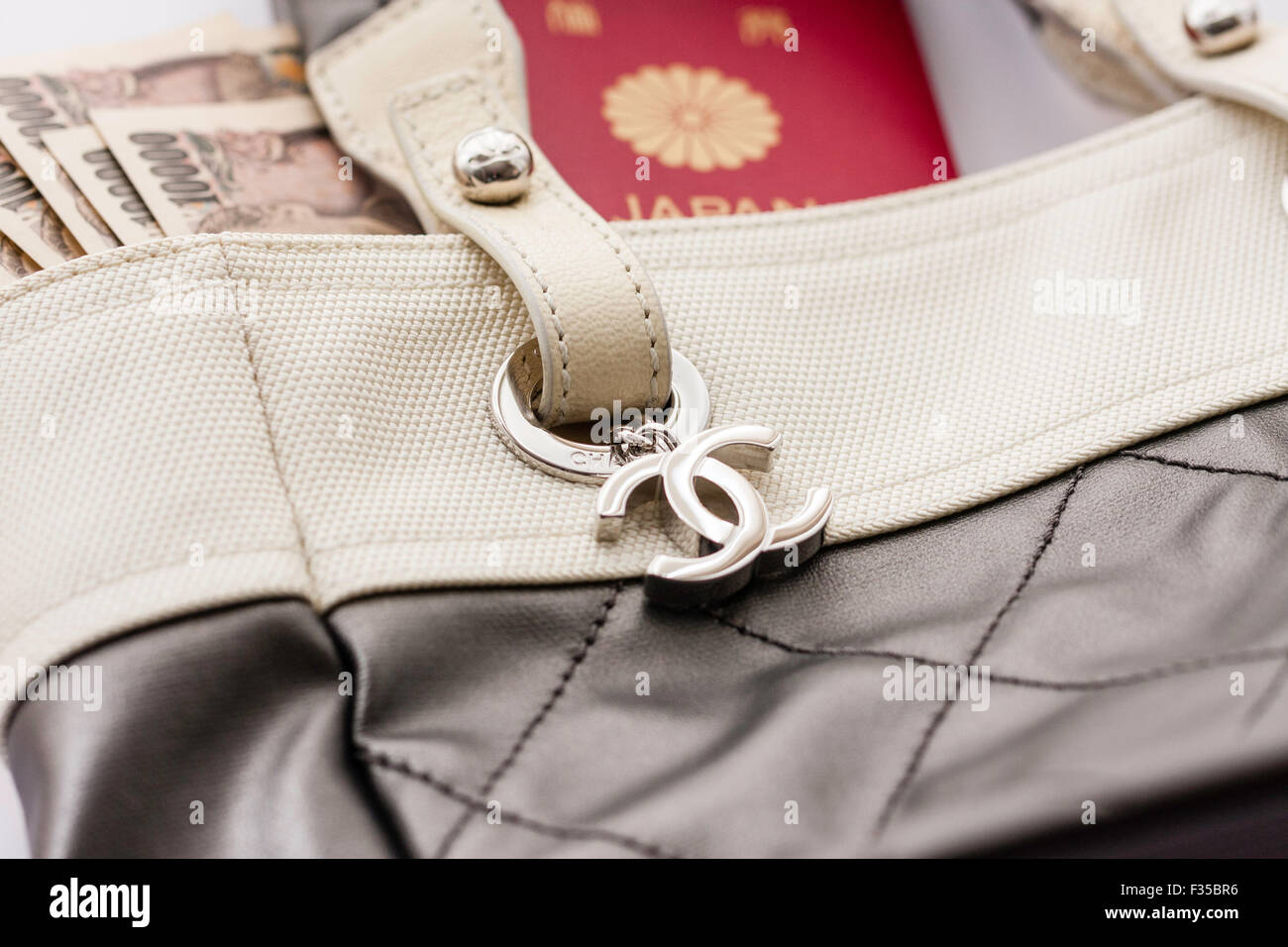 Close up dettaglio di un marchio Chanel nome borsa designer con il suo logo in metallo tag, CC e passaporto giapponese e Yen banconote. Foto Stock