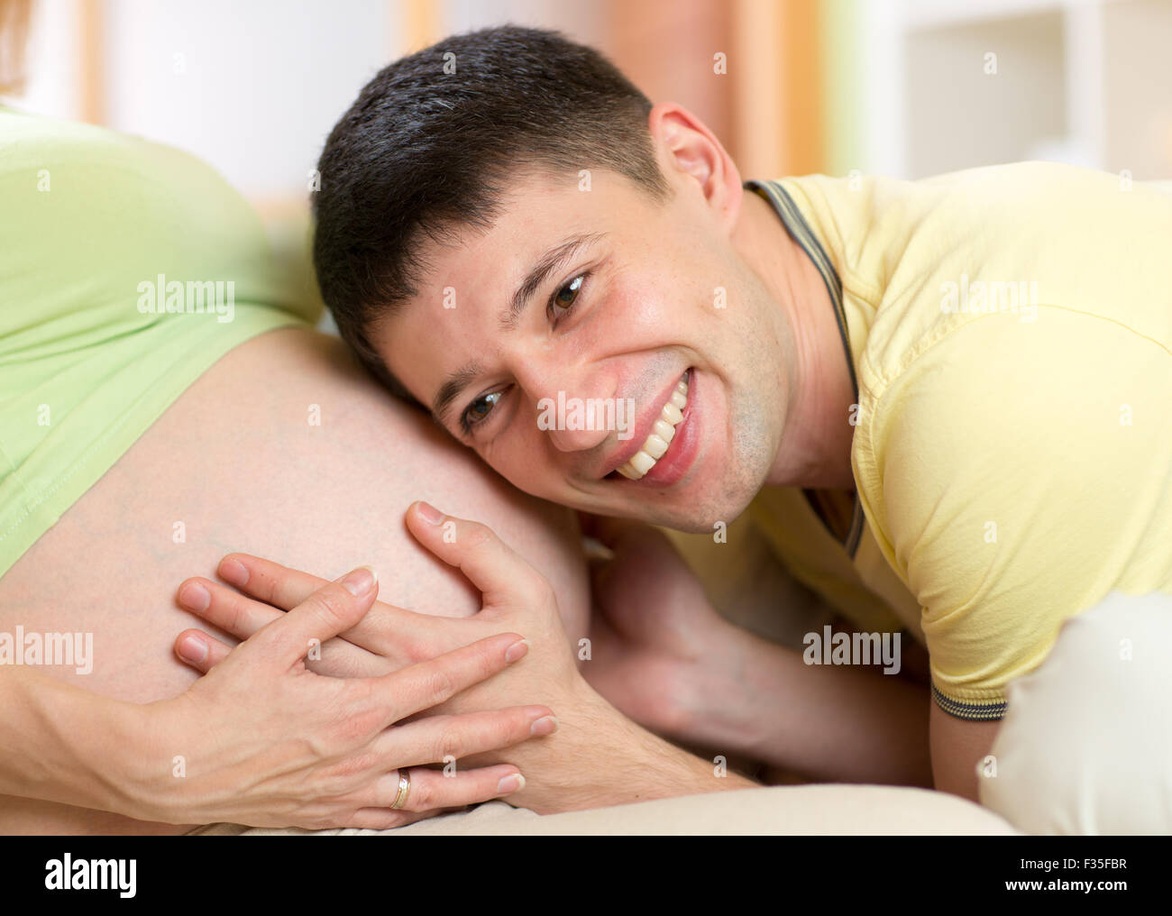 Uomo felice ascoltando la pancia di sua moglie incinta Foto Stock