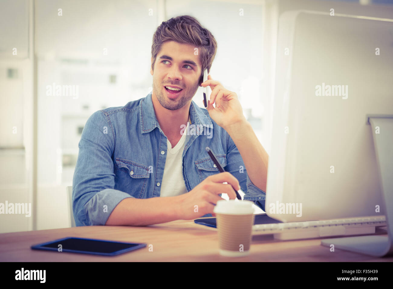 Felice hipster utilizzando il telefono cellulare mentre è seduto alla scrivania Foto Stock