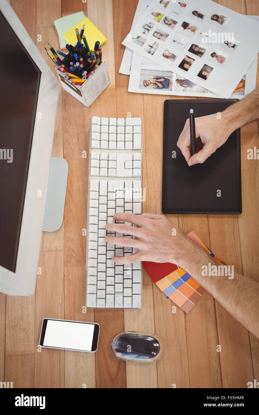 Uomo con tavoletta grafica e computer presso la scrivania in ufficio Foto Stock