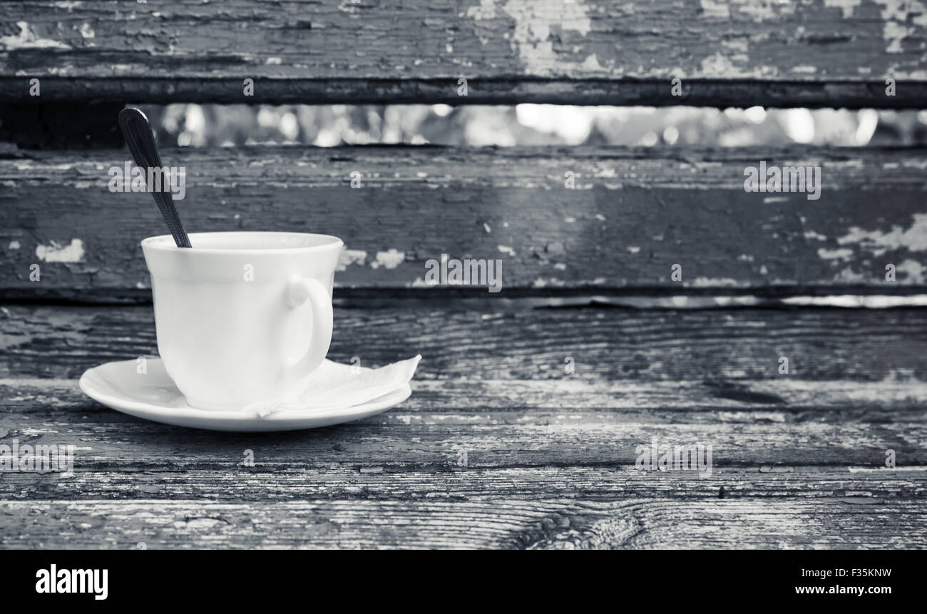 Tazza di caffè è su una vecchia panca di legno in autunno park. Messa a fuoco selettiva con shallow DOF, foto in bianco e nero Foto Stock