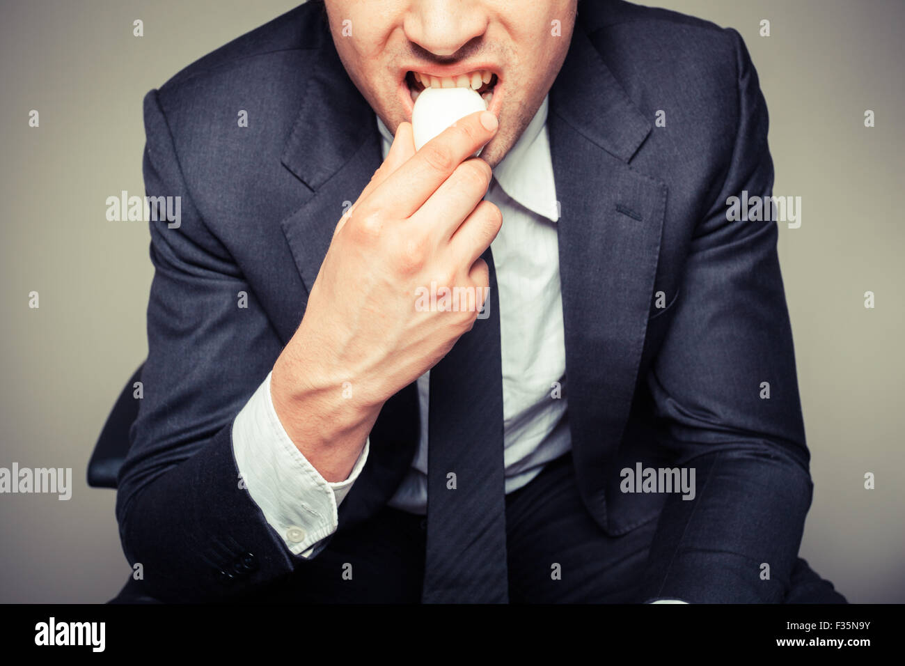 Un imprenditore seduto in una sedia per ufficio è mangiare un uovo Foto Stock