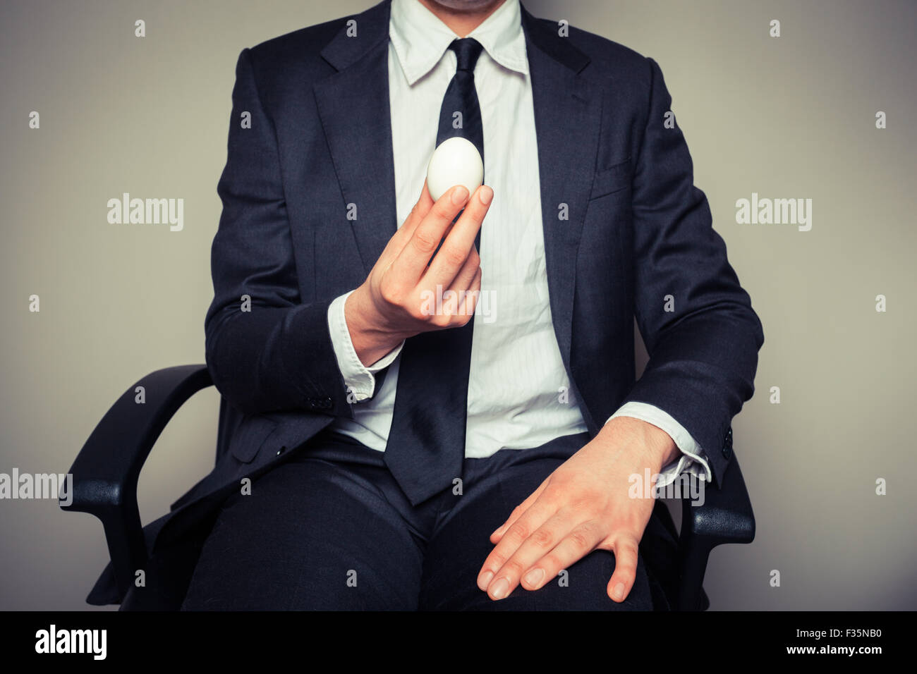 Un giovane imprenditore seduto in una sedia da ufficio è in possesso di un uovo sodo Foto Stock