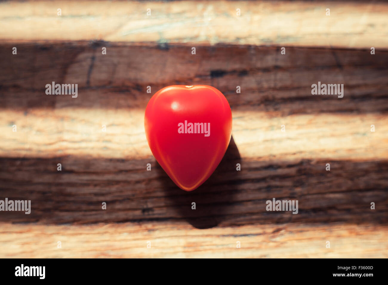 Heartshaped insolita allegra pomodoro su di un tavolo di legno con ombre orizzontale Foto Stock