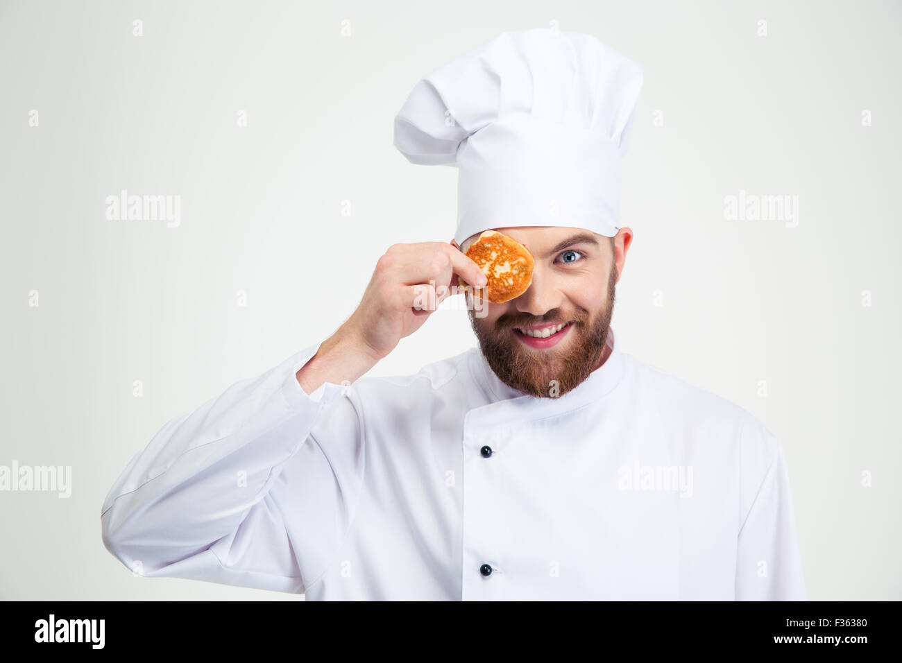 Ritratto di un maschio sorridente chef di cucina che copre il suo occhio con pancake isolato su uno sfondo bianco Foto Stock