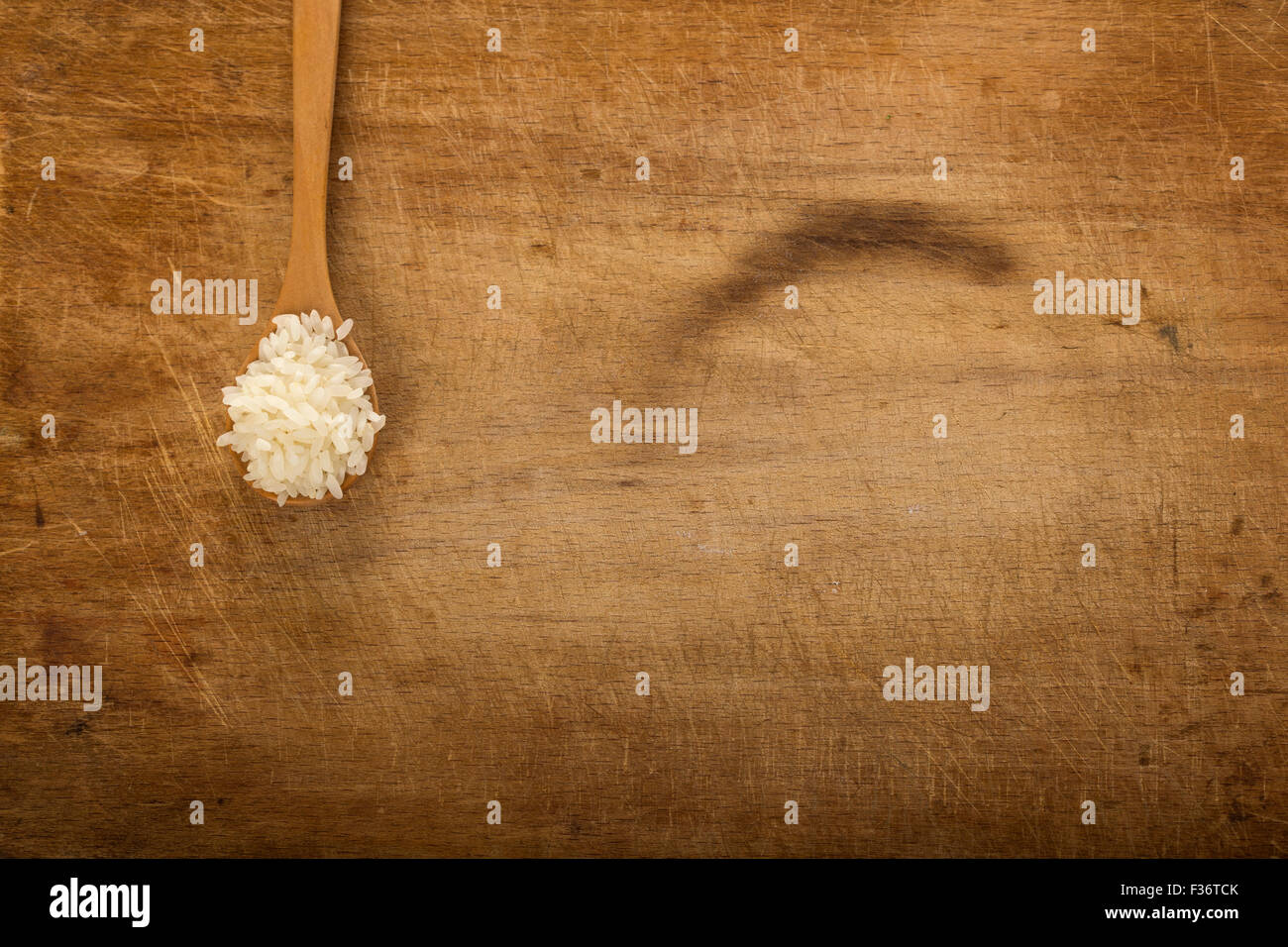 Il cucchiaio di legno con chicchi di riso su sfondo rustico con spazio di copia Foto Stock