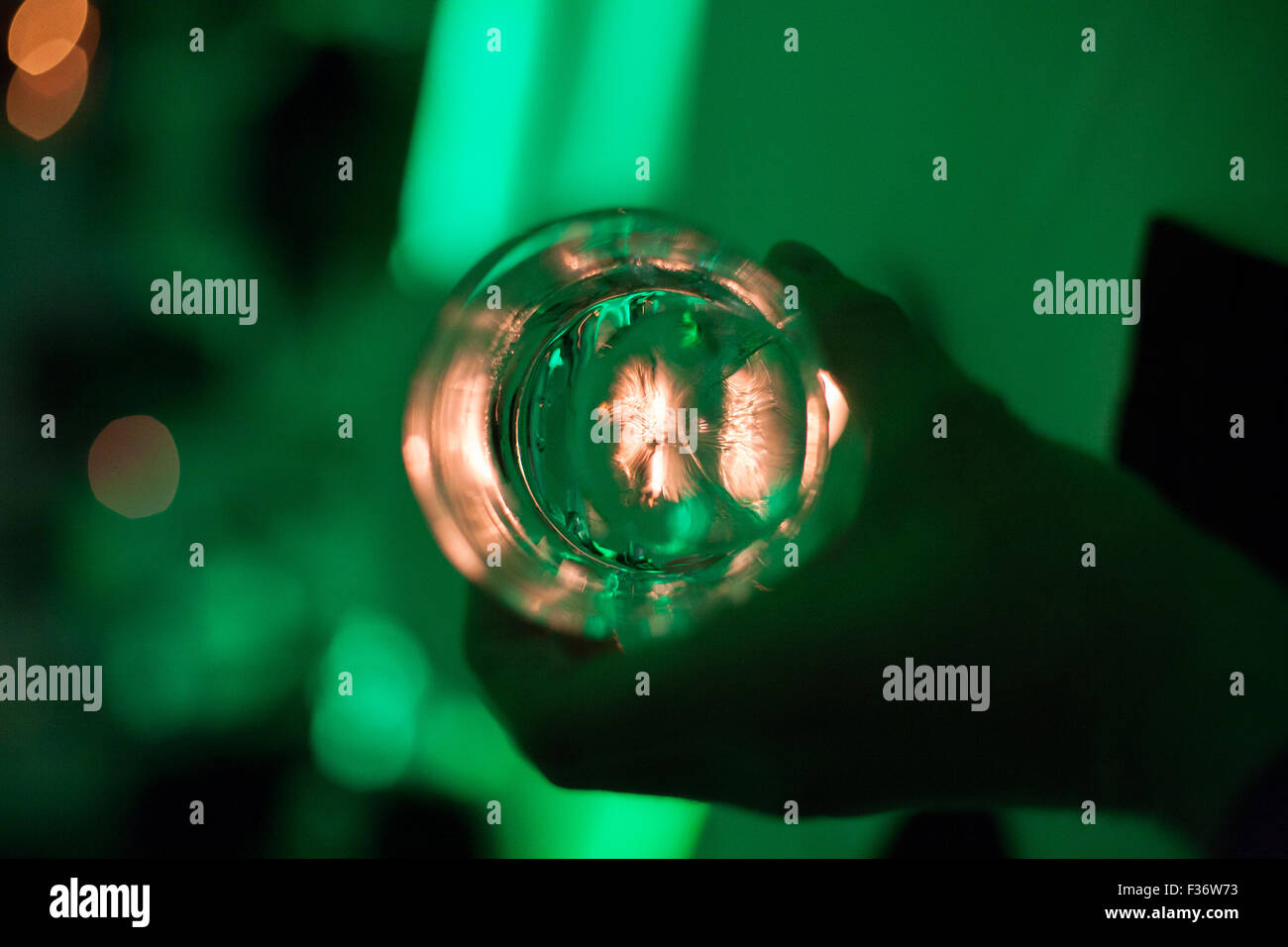 Bagliore verde intorno a mano e bicchiere con ghiaccio e la luce bianca proveniente attraverso il fondo Foto Stock