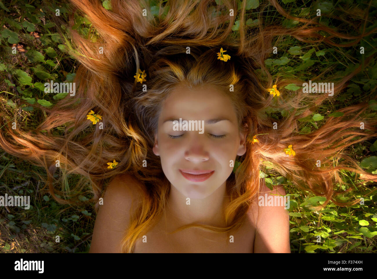 Bella ragazza bionda capelli lunghi in erba con fiori nella sua testa Foto Stock