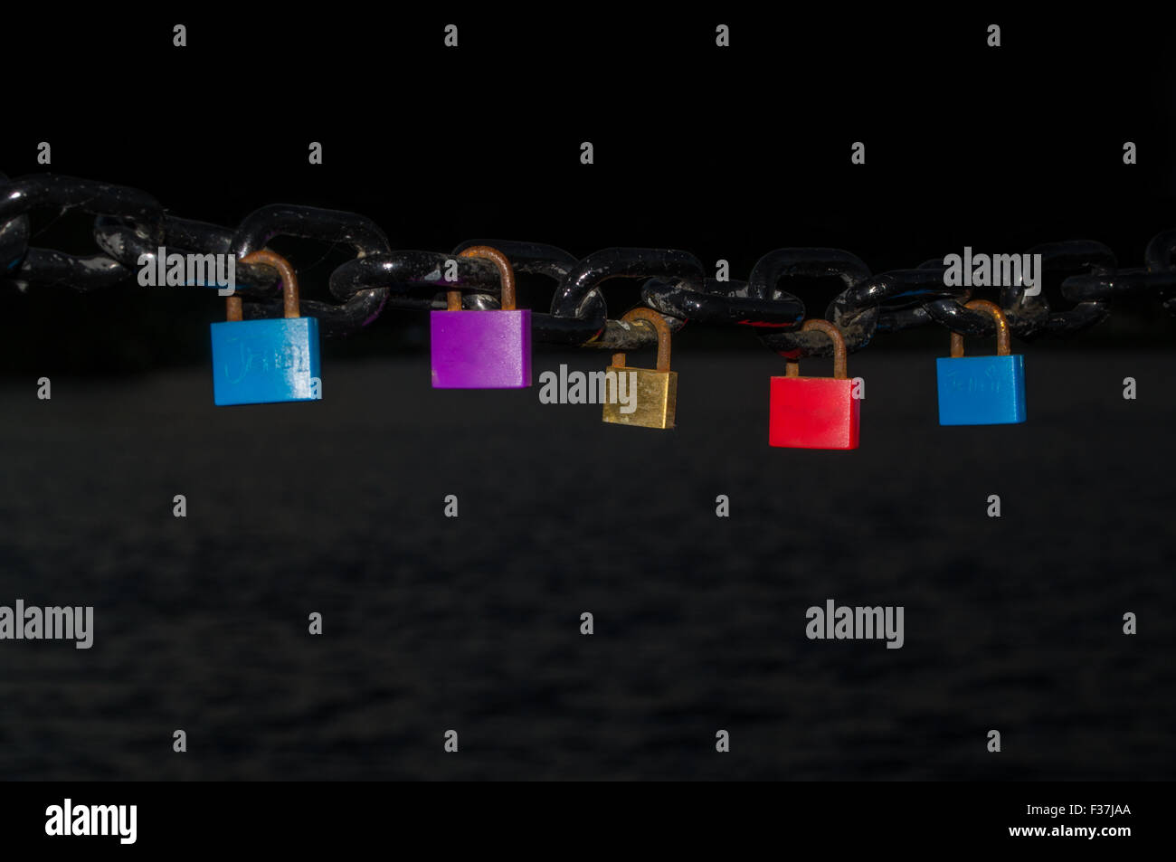 Diversi lucchetti colorati appesi da una catena di nero Foto Stock