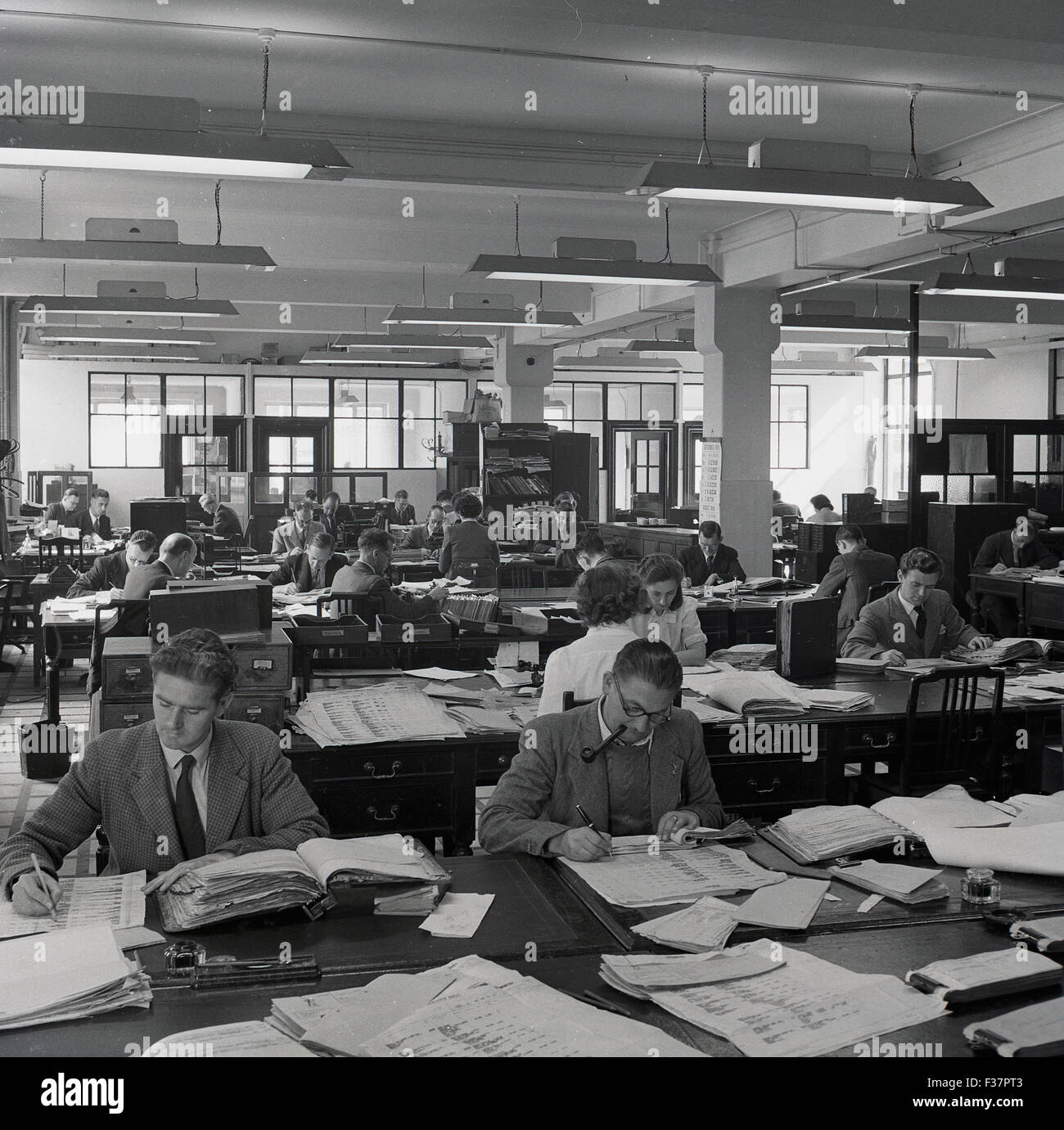 Storico degli anni cinquanta, la foto che mostra un grande ufficio open space con personale di scrivanie unite insieme facendo contabilità, tenuta della contabilità o di lavoro amministrativo. Foto Stock