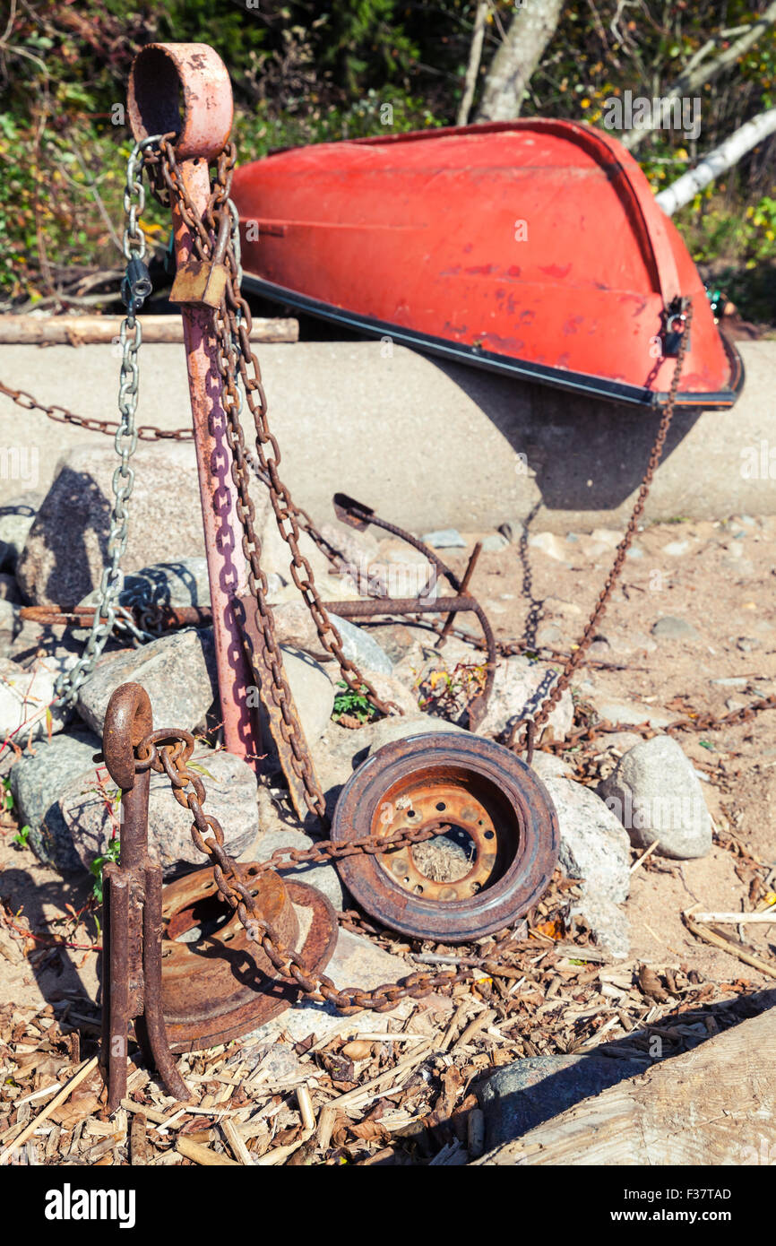 Vecchio rosso canotto giace sulla costa vicino a ancore arrugginite e catene Foto Stock
