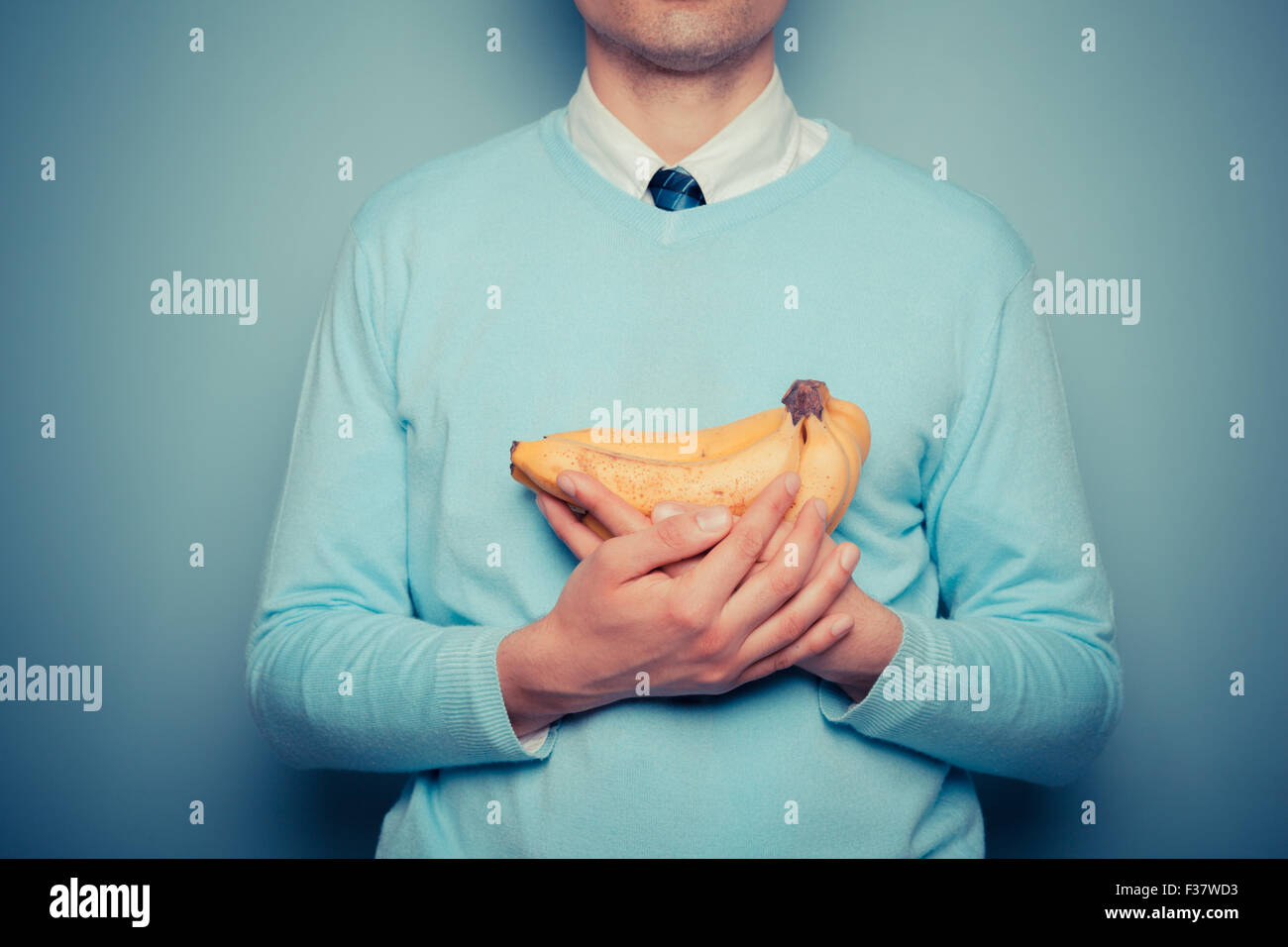 Un giovane uomo tiene in mano un grappolo di banane Foto Stock