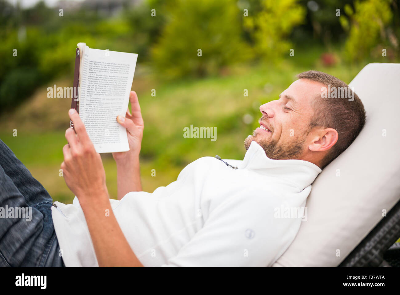 L'uomo la lettura di un libro in poltrona lounge all'aperto. Foto Stock