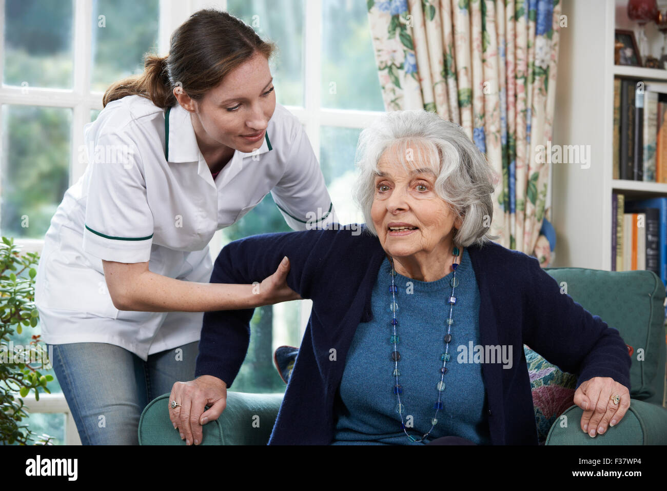 Lavoratore di cura di aiutare la donna Senior per arrivare fino al di fuori della sedia Foto Stock