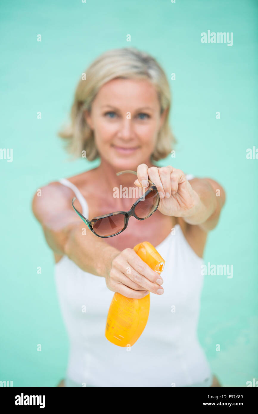 Donna che mantiene gli occhiali da sole e protezione solare. Foto Stock
