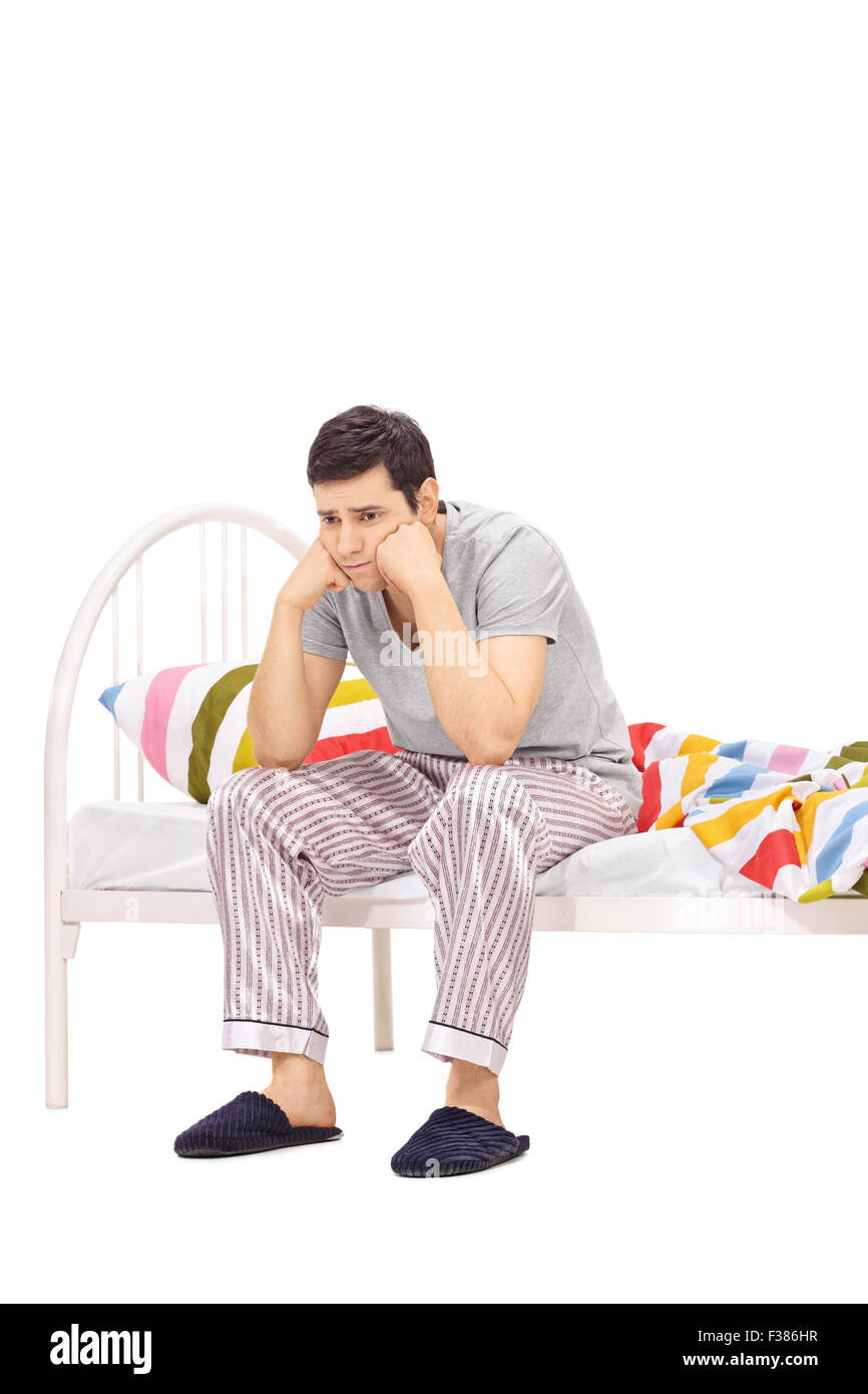 Colpo verticale di un preoccupato per il giovane uomo in pigiama seduto su un letto e contemplando isolati su sfondo bianco Foto Stock