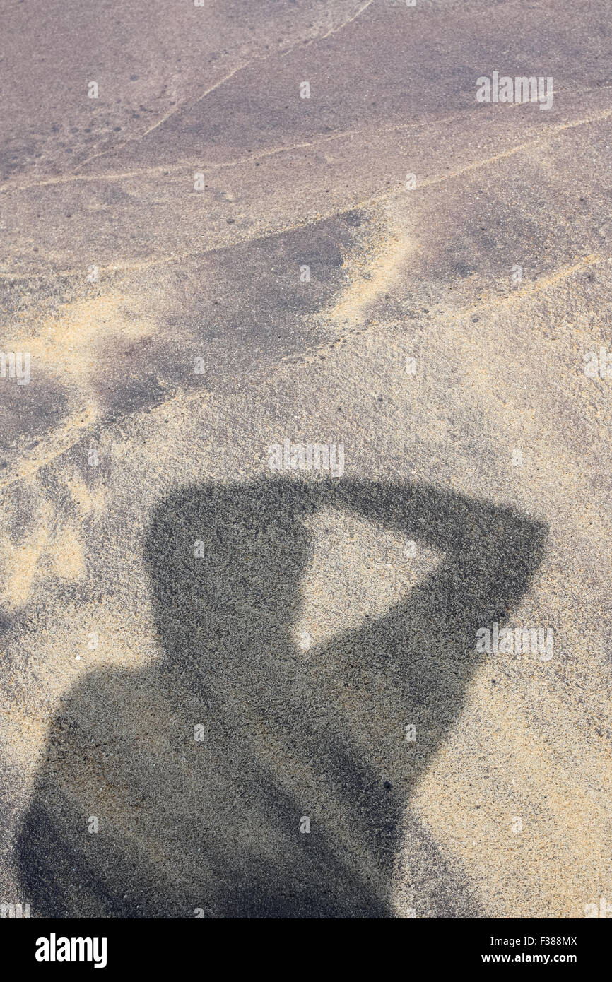 Fotografo ombra su grigio, viola i modelli di spiaggia su una spiaggia tropicale. I modelli creati da forme d'onda arancione con sabbia e limo. Foto Stock