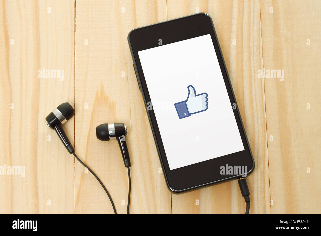 KIEV, UCRAINA - 10 gennaio 2015: Smart phone con Facebook pollice in alto segno sul suo schermo e cuffie su sfondo di legno. Foto Stock