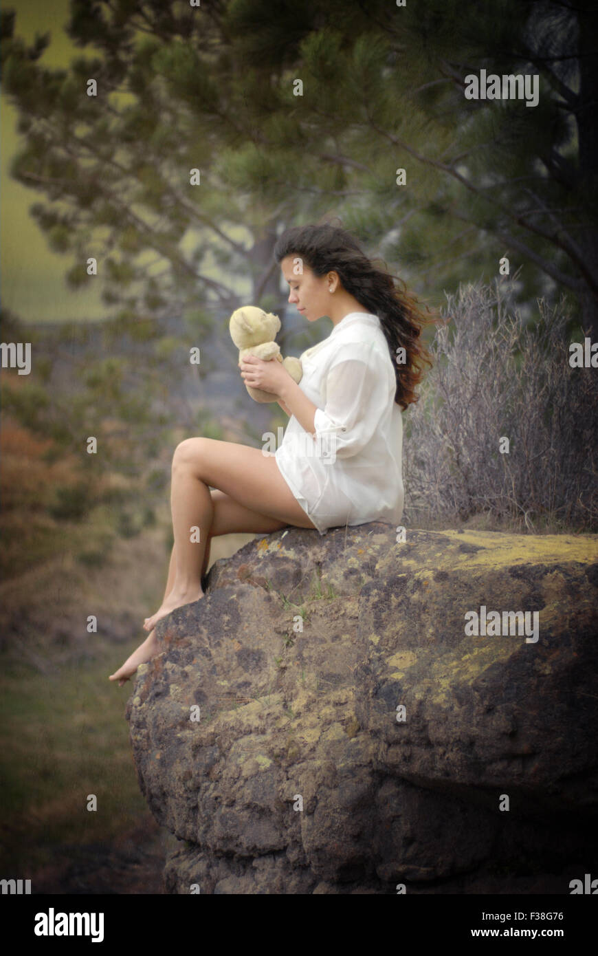Carino ragazza baciare un orsacchiotto seduto in una grossa pietra nella foresta Foto Stock