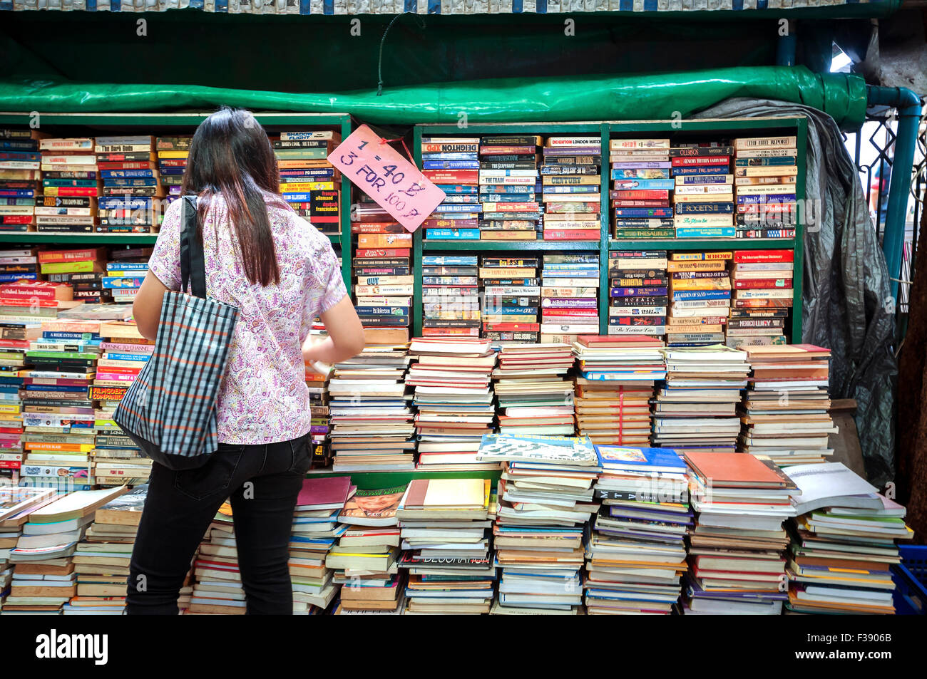 Una ragazza esamina un libro in stallo il Mercato del fine settimana di Chatuchak, Bangkok Foto Stock