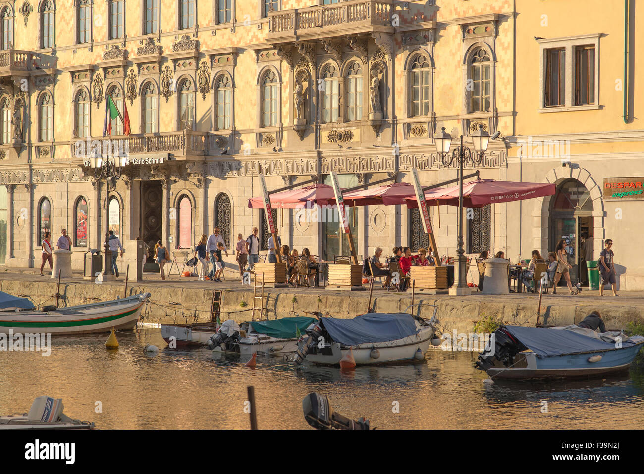 Trieste estate, vista in un pomeriggio d'estate di persone che si rilassano ai tavoli da caffè su una terrazza accanto al Canal Grande di Trieste, Italia. Foto Stock