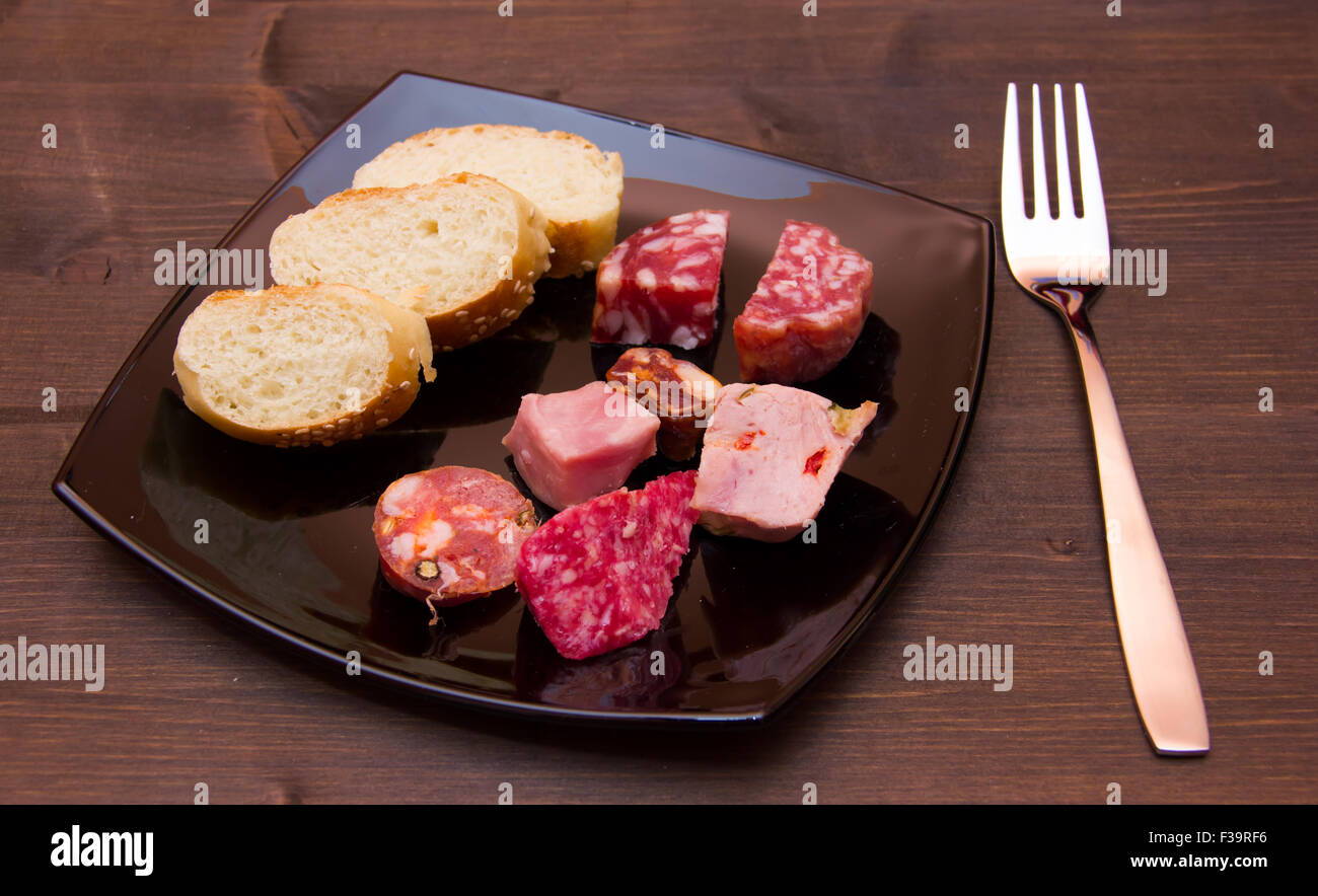 Pezzi di salame e le fette di pane sulla piastra su un tavolo di legno Foto Stock