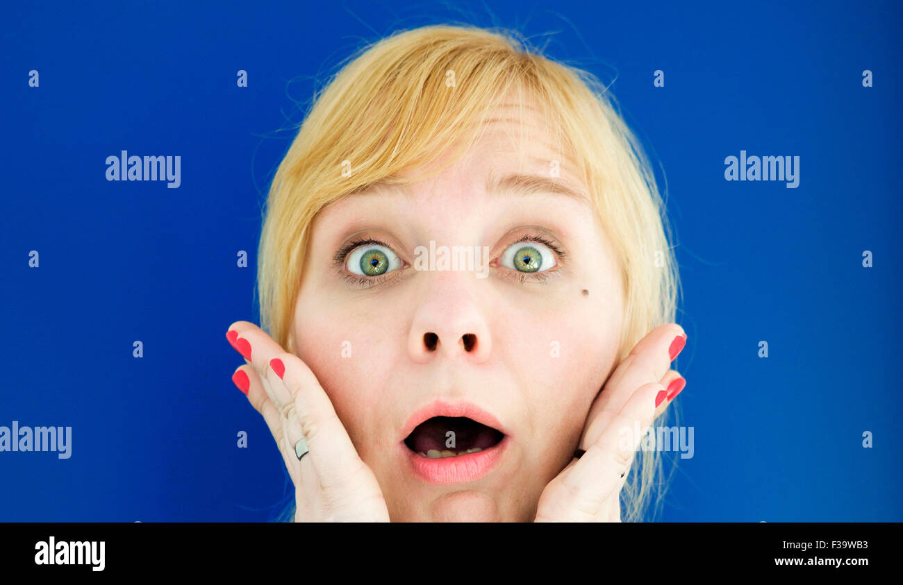 Ritratto di giovane donna bionda su sfondo blu guardando paura e sorpresa Foto Stock