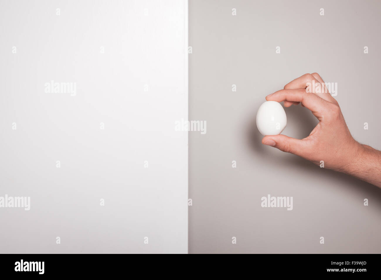 La mano di un uomo è in possesso di un uovo contro un duplice sfondo colorato Foto Stock