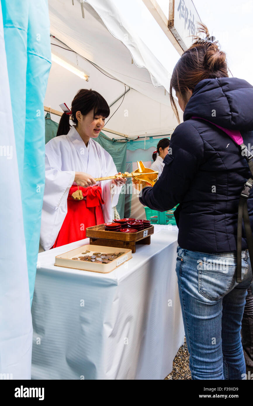 Giappone, sacrario scintoista. Mike, Santuario maiden, spooning out bevande gratuite di saki per persone come parte del nuovo anno la festa a Nishinomiya santuario. Foto Stock