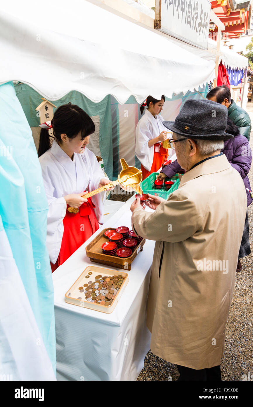 Giappone, sacrario scintoista. Mike, Santuario maiden, spooning out bevande gratuite di saki per persone come parte del nuovo anno la festa a Nishinomiya santuario. Foto Stock
