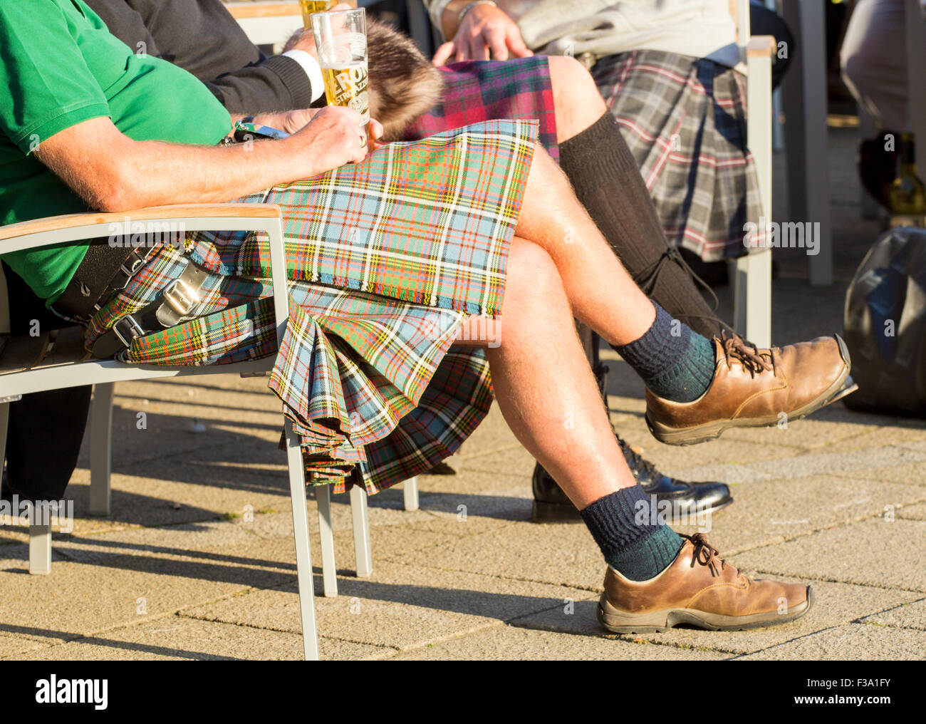 Scottish uomini che indossano kilts gustando una birra al di fuori del pub. Foto Stock