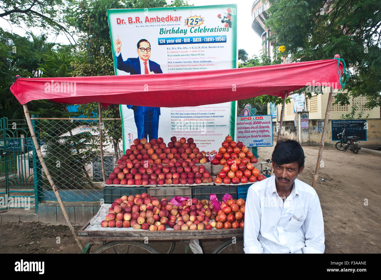 L'uomo vendita di mele e melograni davanti a un cartellone di commemorazione B.R. Ambedkar, un famoso uomo politico indiano leader. Foto Stock