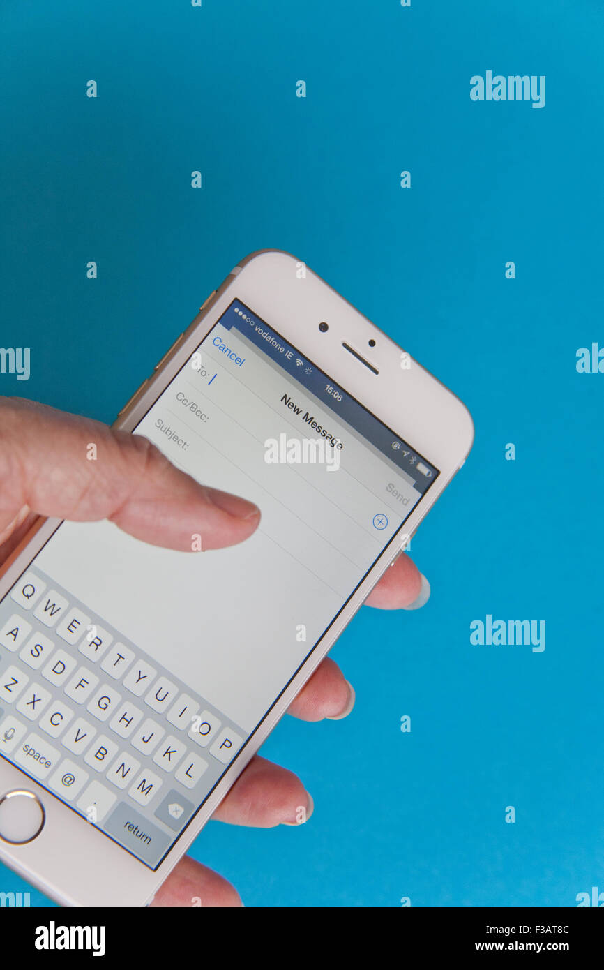 Invio di un messaggio di posta elettronica su un oro e bianco Apple iPhone 6 contro uno sfondo blu Foto Stock