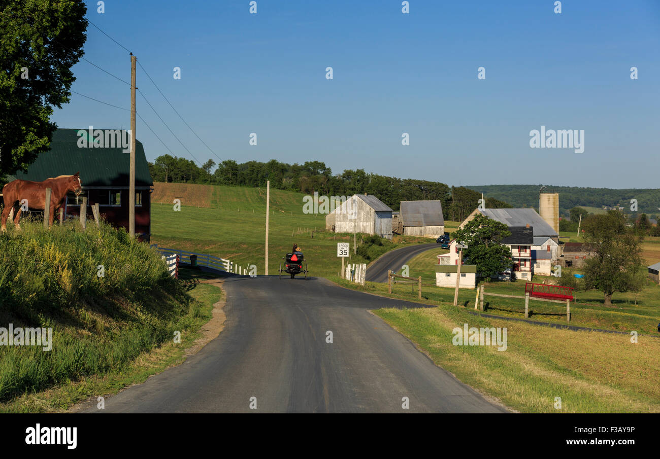 Lancaster County, Pennsylvania Amish cavallo e buggy quadrato sulla strada di campagna passato edifici agricoli Foto Stock