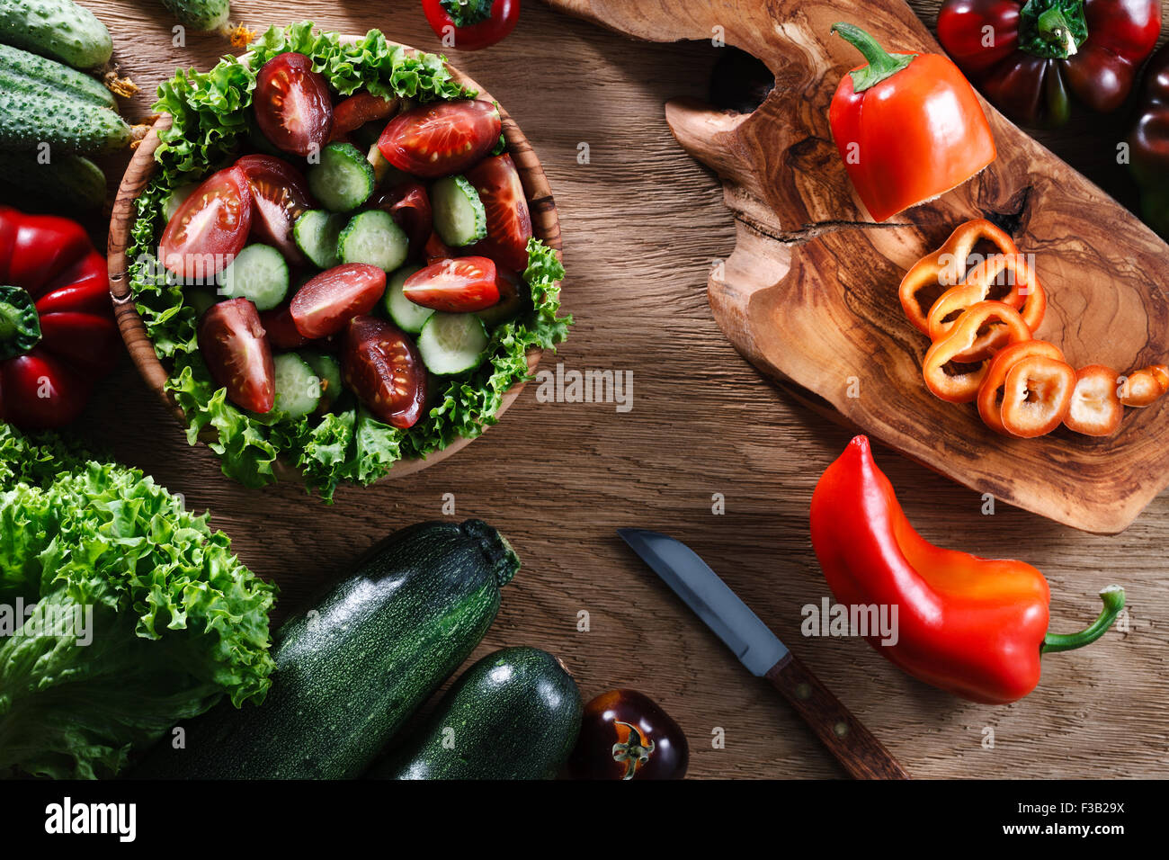 Una ciotola di legno di verdura fresca insalata circondato dagli ingredienti: insalata verde, cetrioli, peperoni, pomodori e marro Foto Stock
