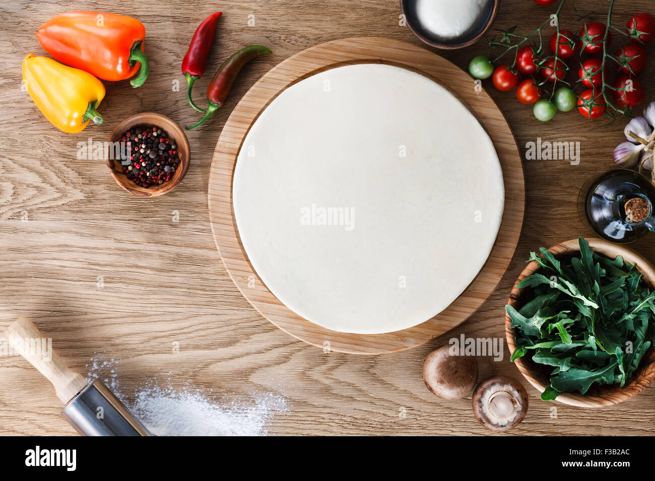 Pasta fresca la base della pizza e gli ingredienti su una trama di legno tabella. Vista dall'alto. Foto Stock