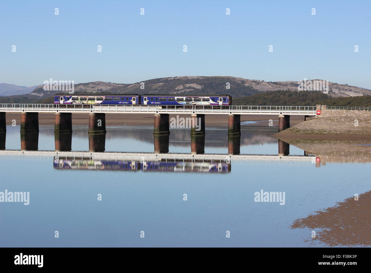 Diesel Multiple Unit treno in livrea settentrionale attraversando Arnside viadotto ad alta marea con la riflessione nel fiume Kent. Foto Stock