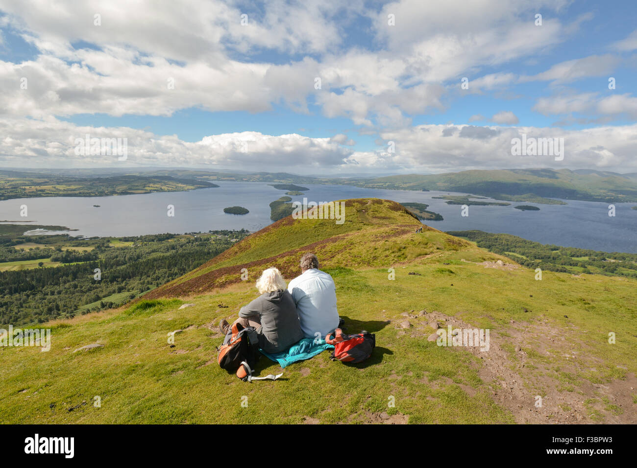 Loch Lomond - Coppia matura seduti sulla collina conica ammirando una vista in elevazione del Loch Lomond, Loch Lomond e il Trossachs National Park, Scozia Foto Stock