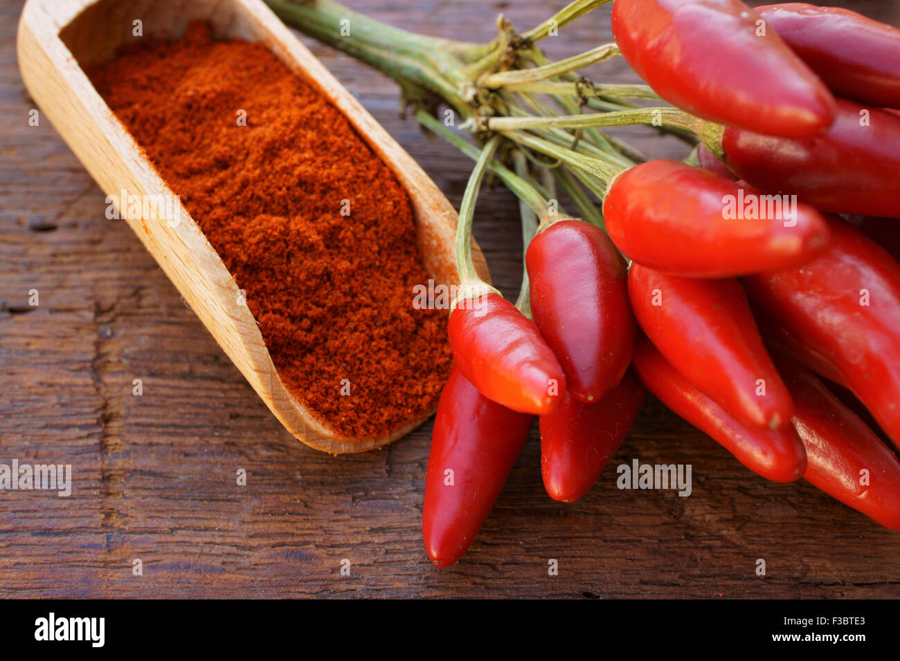 Peperoncino baccello come mazzo e peperoncino in polvere su un di legno spice scoop su una tavola in legno rustico Foto Stock