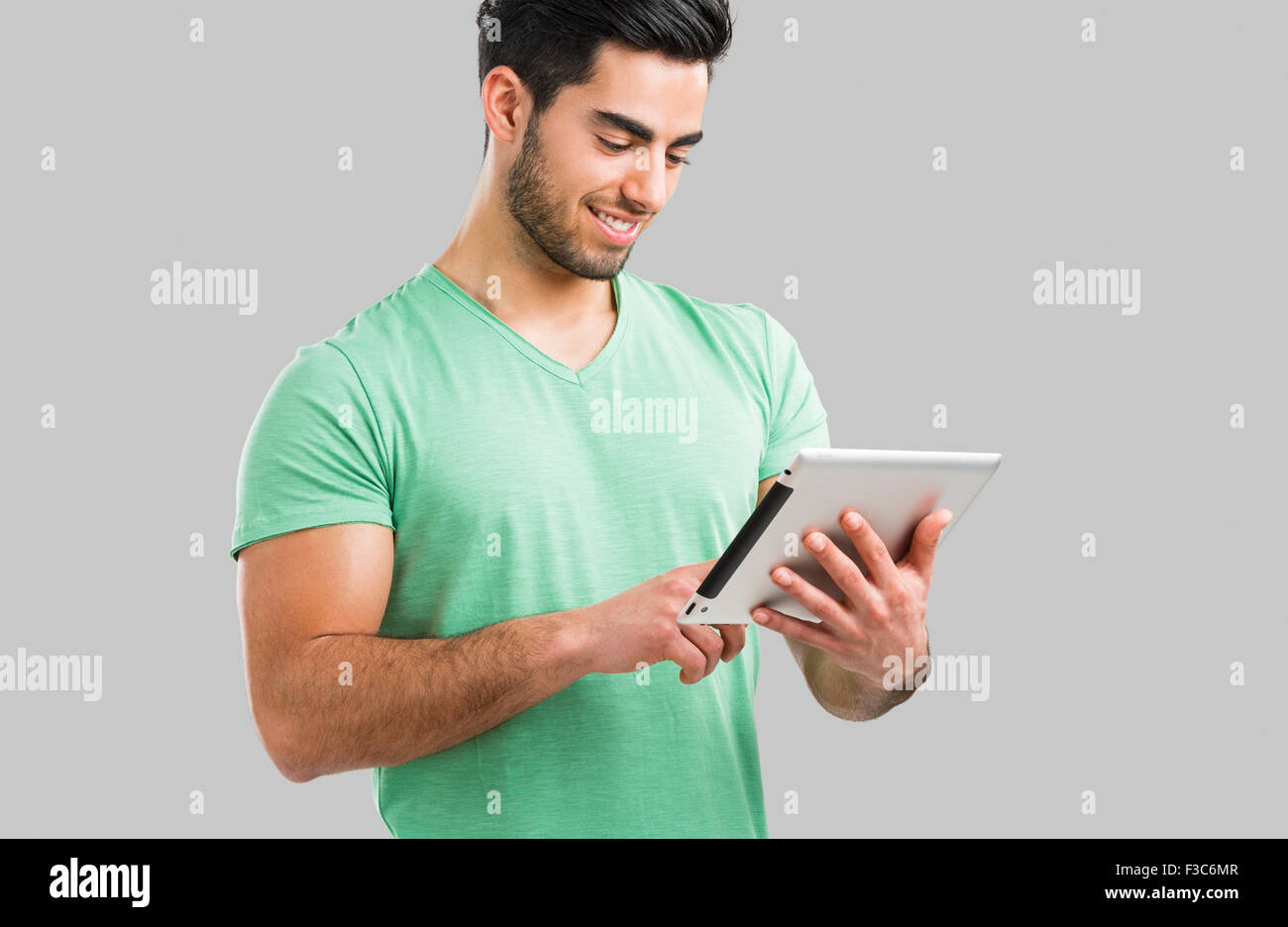 Bel giovane uomo che lavora con una pastiglia, isolate su uno sfondo grigio Foto Stock