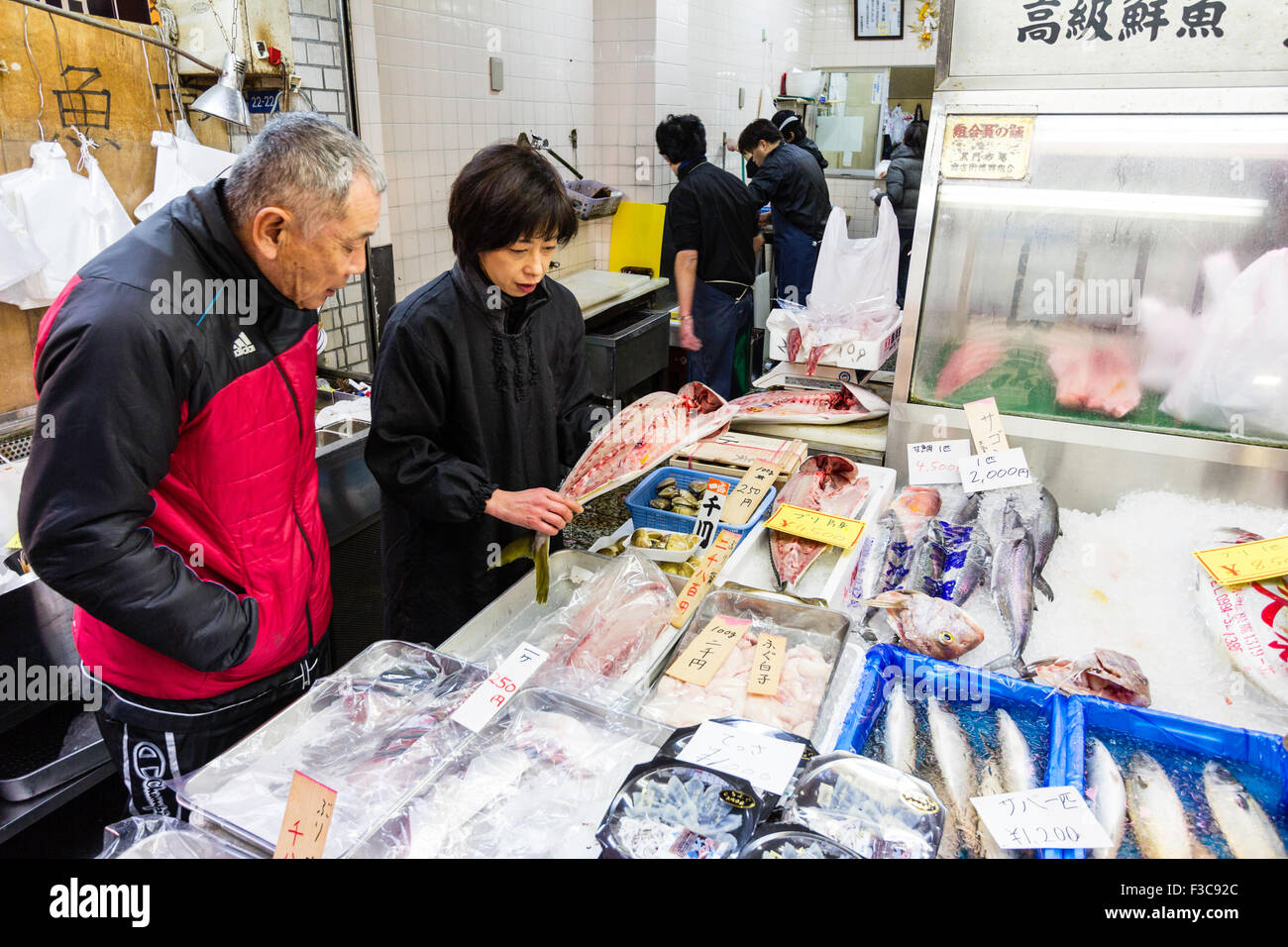 Giappone, Osaka, Kuromon Ichiba mercato, "Osaka cucina", il cliente sta guardando i pesci sono mostrati a lui da assistente vendite donna al tuo pescivendolo stallo. Foto Stock