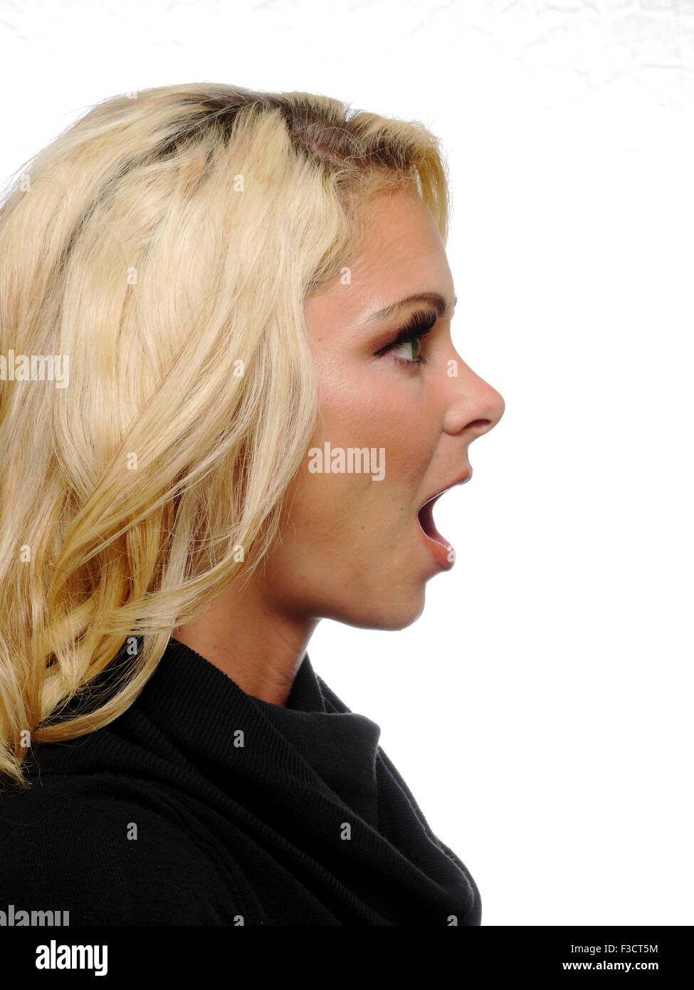 Una testa e spalle vista di profilo di una bionda attraente modello caucasico posa con la bocca aperta in un urlo. Foto Stock