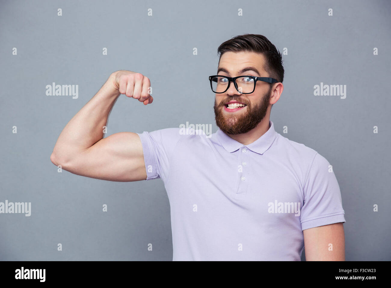 Ritratto di uno strano uomo in bicchieri che mostra i suoi muscoli su sfondo grigio Foto Stock