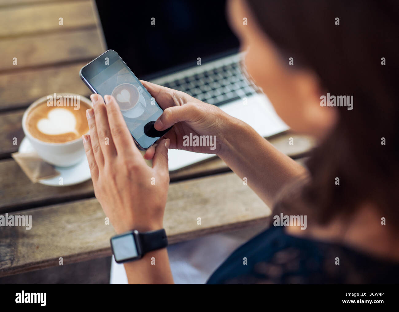 Immagine ravvicinata di donna fotografare un caffè di cup con il suo telefono cellulare mentre è seduto in un bar. Foto Stock